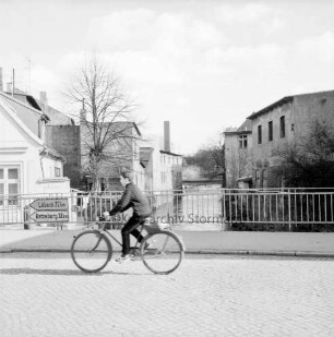 Trave: Stadtarm: vorn Hamburger Torbrücke mit Fahrradfahrer: links Straßenschilder am Geländer: Blick Richtung Lübecker Tor und Heiliggeistviertel: hinten Fußgängerbrücke: rechts und links Gebäude