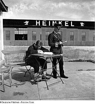 Rostock-Warnemünde. Deutsche Verkehrsfliegerschule, Zweigstelle Seefliegerschule Warnemünde. Ein Angehöriger der Seefliegerschule und ein Luftpolizist (?) auf dem Fluggelände (im Hintergrund Gebäude der Ernst Heinkel Flugzeugwerke)