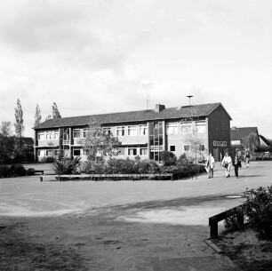 Hauptschule [später: Gertrud-Lege-Schule]: Erweiterungsbau des IV. Bauabschnitts: davor Wege und Grünanlage mit Sträuchern und Bäumen: rechts Gruppe von Schülern: hinten rechts weiteres Schulgebäude: hinten links Wohnblock