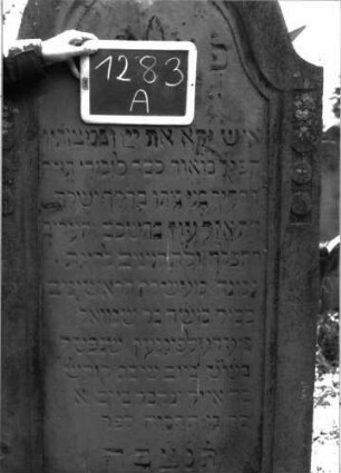 Grabstein 1283 (Index: 100104529) Material: Sandstein Zustand: leicht angewittert Maße HxBxT: 178x75x20 cm Beschreibung: Stele mit Konvexbogenabschluss, Schriftfeld eingetieft, im Bogenfeld Blüte, auf dem Rahmen Scheibenfries, Buchstaben wurden mit schwarzer Farbe nachgezogen, nur noch Reste erhalten Symbolik: Blüte, Scheibenfries: Grabstein 1283A