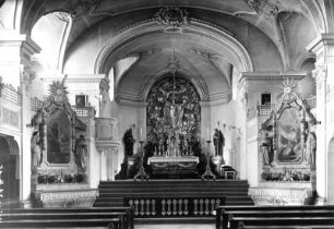 Inneres einer Klosterkirche. Blick über die Seitenaltäre in den Chor zum Hauptaltar mit Metallrelief "Mariä Himmelfahrt"