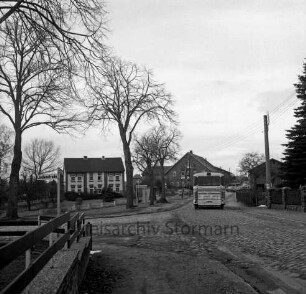 Dorfstraße: Kreisstraße zwischen Bad Oldesloe und Tremsbüttel: Kopfsteinpflaster und Schlaglöcher: links Abzweigung der Lindenstraße mit Bäumen: hinten rechts Bus: im Hintergrund Bauernhäuser und Wohnhaus