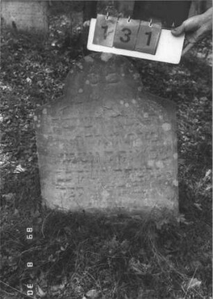 Grabstein 131 (Index: 99609767) Material: Sandstein Zustand: stark verwittert, weitgehender Textverlust Maße HxBxT: 64x57x9 cm Beschreibung: Stele, schräg eingezogener Rundbogenabschluß: Grabstein 131