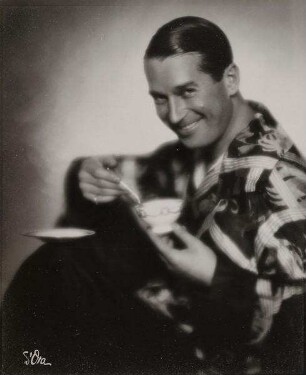 Maurice Chevalier im Seidenpyjama mit Teetasse