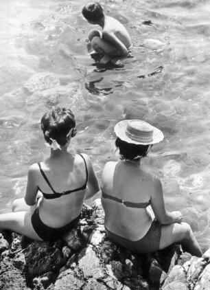 Urlaub an der Adria im Veneto. Frauen sitzen am steinigen Strand. Eine Junge befindet sich im Wasser