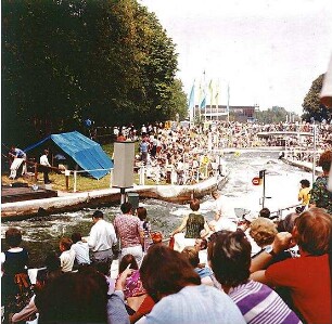 Hansjakob, Gottfried; Augsburg - Spickel, Am Eiskanal 30A; Kanuslalom Olympiastrecke, Freiflächengestaltung - Wettkampfstrecke während Olympiade, Tribünen und Brücke mit Zuschauern, Blick Richtung Norden