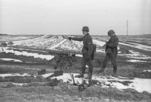 Zwei Wehrmachtsangehörige neben einem Maschinengewehr an einem Feld