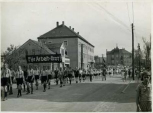 Arbeitersportlerinnen und Arbeitersportler mit dem Transparent "Für Arbeit und Brot!" vor der Drogerie Thürmer in Heidenau