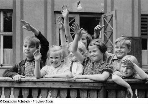 Lachende und winkende Kinder an einer Brüstung