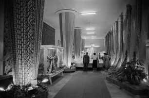 Besucher der Leipziger Herbstmesse 1955 betrachten drapierte Stoffbahnen