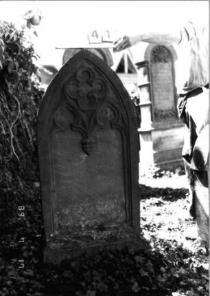 Grabstein 41 (Index: 99798246) Material: Sandstein, rot Zustand: stark verwittert Maße HxBxT: 123x56x11 cm Beschreibung: Stele, Spitzbogenabschluß, Sockel Symbolik: Maßwerk: Grabstein 41