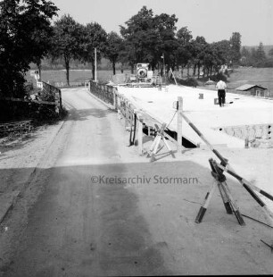 Trave: Brückenneubau: Spannbetonbrücke: Rohbau: links alte Holzbrücke: hinten Bauarbeiter und Baumaschine: dahinter Allee
