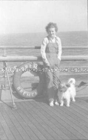 Junge Frau mit Hund an Deck des Hochseepassagierdampfers "Bremen", neben einem Rettungsring an der Reling lehnend