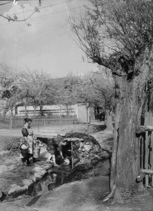 Mutter mit zwei Kindern an einem Brunnehaus Wasser holen