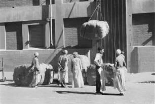 Reisefotos. Arbeiter an einem Flaschenzug mit Ballen vor einem Speichergebäude im arabischen Raum (wahrscheinlich in einem Hafen)