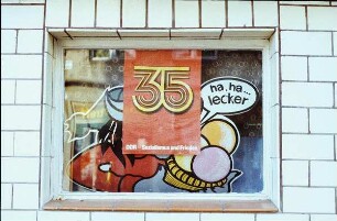 DDR. Fenster einer Speiseeis-Verkaufsstelle mit Aufkleber "ha, ha...lecker" und mit Plakat zum 35. Jahrestag der Gründung der DDR "35 DDR - Sozialismus und Frieden"