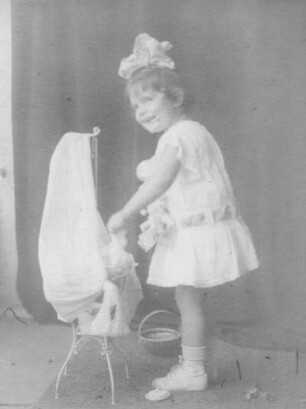 Album mit Porträtserie eines kleinen Mädchens. Mädchen im Sommerkleid, neben einem Puppenbett stehend