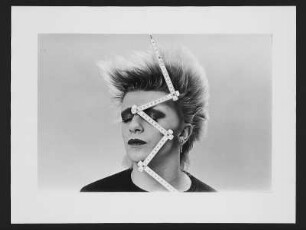 Zollstock : Porträt des New Wave-Musikers Mark A. Defris im Halbprofil, ein Zollstock über das Gesicht gelegt