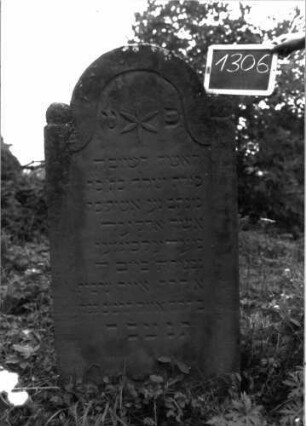 Grabstein 1306 (Index: 100104575) Material: Sandstein Zustand: gut erhalten, unten beginnende Verwitterung Maße HxBxT: 143x67x10 cm Beschreibung: Stele mit eingezogenem Rundbogenabschluss, auf den Einzügen Kugelaufsätze, Schriftfeld eingetieft mit Konvexbogenabschluss, im Bogenfeld Blüte Symbolik: Blüte: Grabstein 1306