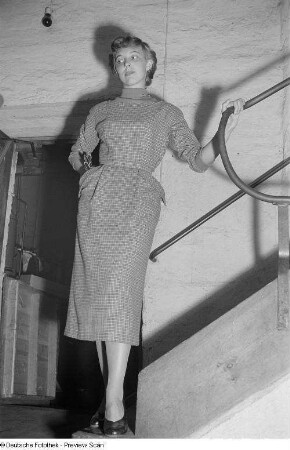 Eine Frau posiert mit einem Kleid an einer Treppe bei der "Internationalen Messemodenschau", Herbstmesse 1953