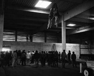 Gewerbebetrieb: Halle: Richtfest: Innenaufnahme: unter Decke Richtkrone: auf Zwischenmauer Polier beim Verlesen des Richtspruchs, Handwerker: Richtgäste: Leiter, Gerüstteile, vorne rechts Wagen
