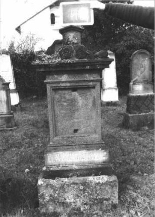 Grabstein 48 (Index: 100112267) Material: Sandstein Zustand: verwittert, Schriftplatte fehlt Maße HxBxT: 152x41x22 cm Beschreibung: Stele, getreppter Sockel, Abdeckplatte mit Volutenaufsatz mit Turmaufsatz, rechteckige Schriftplatte: Grabstein 48