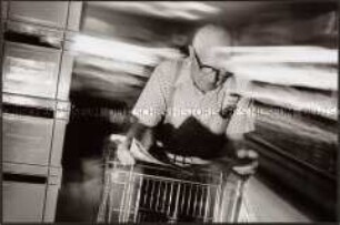 Rentner stützt sich im Supermarkt auf seinen Einkaufswagen und studiert eine Broschüre mit den Sonderangeboten (Sonderthema: Essen und Trinken)