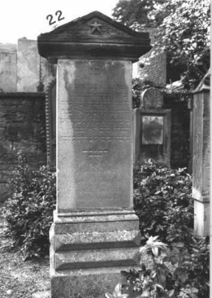 Grabstein 22 (Index: 100114434) Material: Kalkstein, Giebel: Sandstein Zustand: leicht verwittert Maße HxBxT: 175x63x26 cm Beschreibung: Stele, getreppter Sockel, Giebel Symbolik: fünfzackiger Stern Besonderheit: Giebel gehört vermutlich nicht zum Stein: Grabstein 22