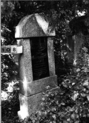 Grabstein 108 (Index: 99792656) Material: Granit, Glasplatte Zustand: gut, Platte quer gesprungen Maße HxBxT: 182x66x23 cm Beschreibung: Stele, getreppter Sockel, eingezogener Rundbogenabschluß, rechteckige Schriftplatte: Grabstein 108