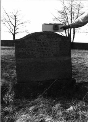 Grabstein 6 (Index: 100116078) Material: Granit Zustand: gut Maße HxBxT: 107x90x14 cm Beschreibung: aufgesockelte, breite Stele mit eingezogenem Segmentbogenabschluß: Grabstein 6