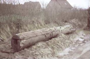 Moorweg: bei Durchlass Alte Alster: Fundstück Rohrleitung aus Holz, nach Bergung: Gesamtansicht, längs darauf Zollstock zum Größenvergleich, vorne Querschnitt: hinten rechts Bagger [angeschnitten]: im Hintergrund Häuser