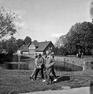 Dorfstraße: Dorfteich: vorn Mitte Gruppe Jugendlicher: links Birke: dahinter Springbrunnen: hinten rechts Personengruppe: im Hintergrund Bäume und Häuser