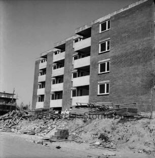 Ehmkenberg: Neubau: Wohnblock vor Fertigstellung: vorn Stapel mit Gerüsten, Erdhaufen, Bauschutt, Stromleitung, Ziegelstapel: hinten links Wohnblock