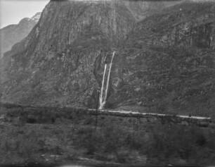 Wasserfall : Ein Wasserfall strömt von einem Berg hinab, im Vordergrund ebenes Land