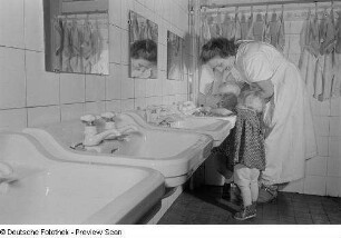 Zwei Kleinkinder und eine Erzieherin an einem Waschbecken eines Kinderkrippenbaderaum