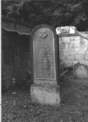 Grabstein 110 (Index: 99609746) Material: Sandstein Zustand: stark verwittert, teilweise Textverlust Maße HxBxT: 165x56x22 cm Beschreibung: Stele, Rundbogenabschluß, Schriftfeld eingetieft, im Bogen vierblättrige Blüte, Sockel Symbolik: Blüte: Grabstein 110