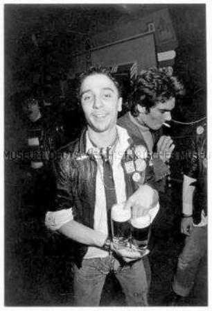 Junger Mann in Lederjacke mit Punk-Pins trägt zwei Gläser Bier (Altersgruppe 14-17)