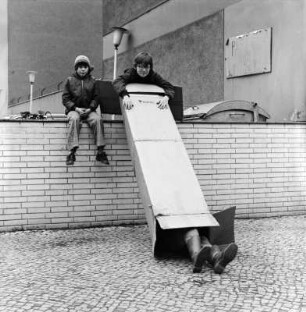Kinder auf einer Mauer machen Jux mit einem Pappkarton