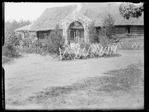 Unbekannte Ortschaft [Litauen/Weißrussland/Ukraine?]: reetgedecktes Holzhaus mit Jägerzaun, Veranda und Empfangsbogen aus Birkenholz