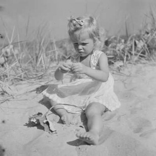 Kleines Mädchen mit Kleid sitzt und spielt am Strand