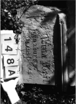 Grabstein 148 (Index: 99792748) Material: Sandstein Zustand: verwitt/Textverl/Plat. fehlt/Sock. beschäd Maße HxBxT: 178x60x25 cm Beschreibung: Stele, profilierter Sockel, Giebel, rechteckiges Schriftfeld eingetieft Symbolik: Felderfries: Grabstein 148A