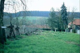 Friedhof und Friedhofsmauer, zwei eiserne Grabkreuze lehnen an der Friedhofsmauer