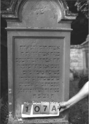 Grabstein 107 (Index: 99609743) Material: Sandstein Zustand: verwittert Maße HxBxT: 204x68x30 cm Beschreibung: Stele, eingezogener Rundbogenabschluß mit Verdachung, Mittelpalmette, vorderes Schriftfeld rechteckig eingetieft, hinteres Schriftfeld plakettenförmig erhaben, getreppter Sockel: Grabstein 107A
