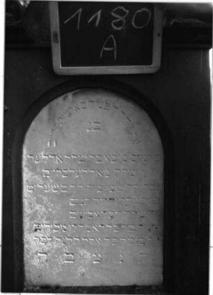 Grabstein 1180 (Index: 100104324) Material: Sandstein, Marmortafel Zustand: gut erhalten, im Giebel beginnende Verwitterung Maße HxBxT: 198x57x22 cm Beschreibung: Stele auf getrepptem Sockel, giebelartiger, hochgezogener Abschluss mit Eck- und Giebelakroterien (Voluten- u. Blattornamente), eingetieftes, rundbogiges Schriftfeld Symbolik: Blattornamente: Grabstein 1180A