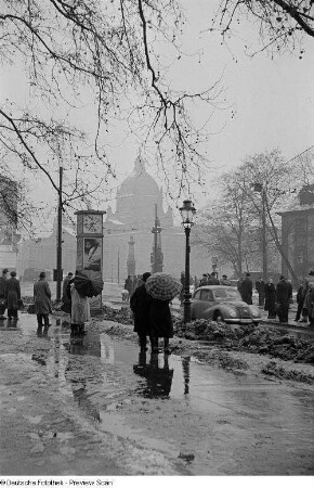 Menschen mit Regenschirmen warten an der Straßenbahnhaltestelle auf dem Martin-Luther-Ring