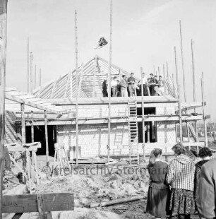 Volksschule Tannenweg: zweiter Erweiterungsbau mit zwei Pavillons: Richtfest: vorn rechts Schülerinnen: dahinter Sandhaufen und Baumaterial: oben auf Dachstuhl Arbeiter