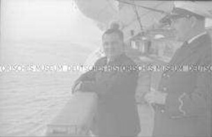 Offizier an Bord des Hochseepassagierdampfers "Bremen", neben einem Passagier an der Reling unter einem Rettungsboot stehend