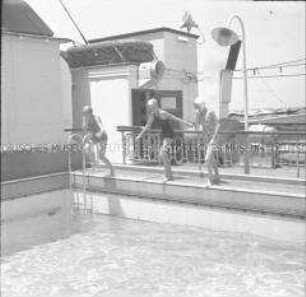 Drei Damen beim Sprung ins Schwimmbecken des Hochseepassagierdampfers "Columbus"