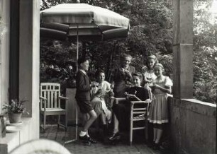 Villa mit Garten. Gruppe von jungen Leuten mit Kompottschalen auf dem Balkon