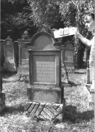 Grabstein 92 (Index: 99609728) Material: Sandstein Zustand: verwittert Maße HxBxT: 170x63x31 cm Beschreibung: Stele, eingezogener Rundbogenabschluß mit Verdachung, Mittelpalmette, Schriftfeld rechteckig eingetieft, getreppter Sockel, unten Rusticaimitat: Grabstein 92